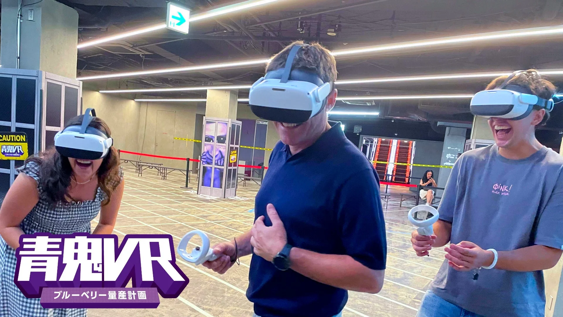 VRヘッドセットを装着した3人が、コントローラーを手に笑顔でゲームを楽しんでいる様子です。活気あるVR体験施設で、背景には「青鬼VR」の看板が見えます。
