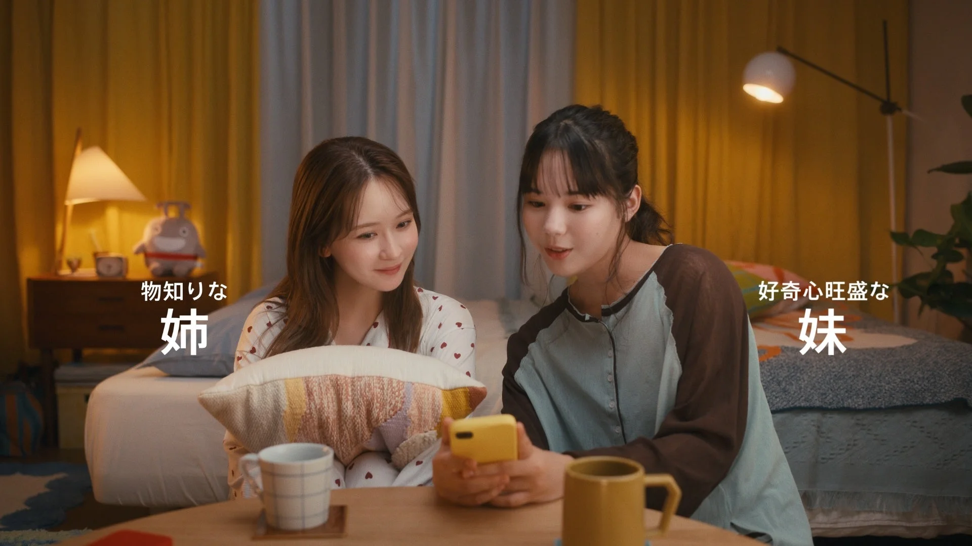 夜の部屋で、パジャマ姿の姉妹がスマートフォンを見ながらくつろいでいる様子