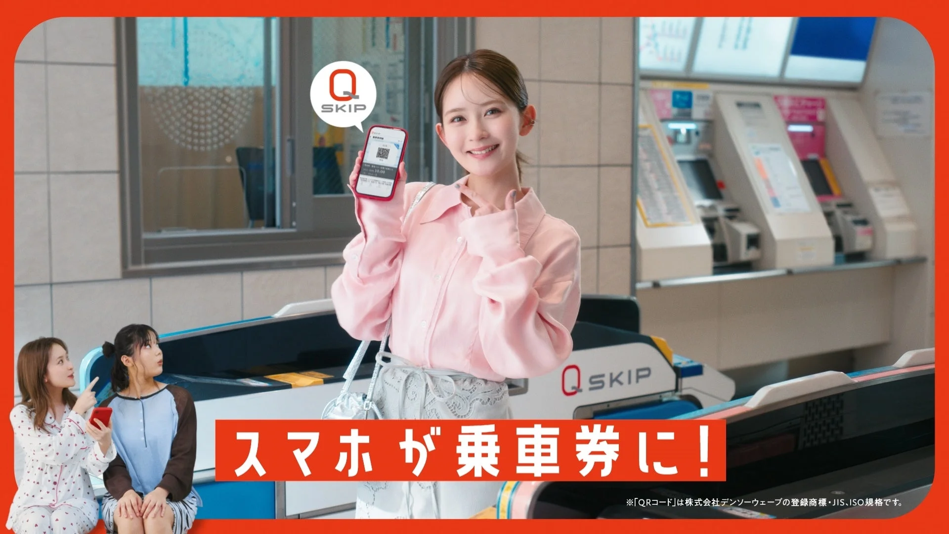 駅の改札前で、スマートフォンをかざして笑顔を見せる女性が中心に描かれています