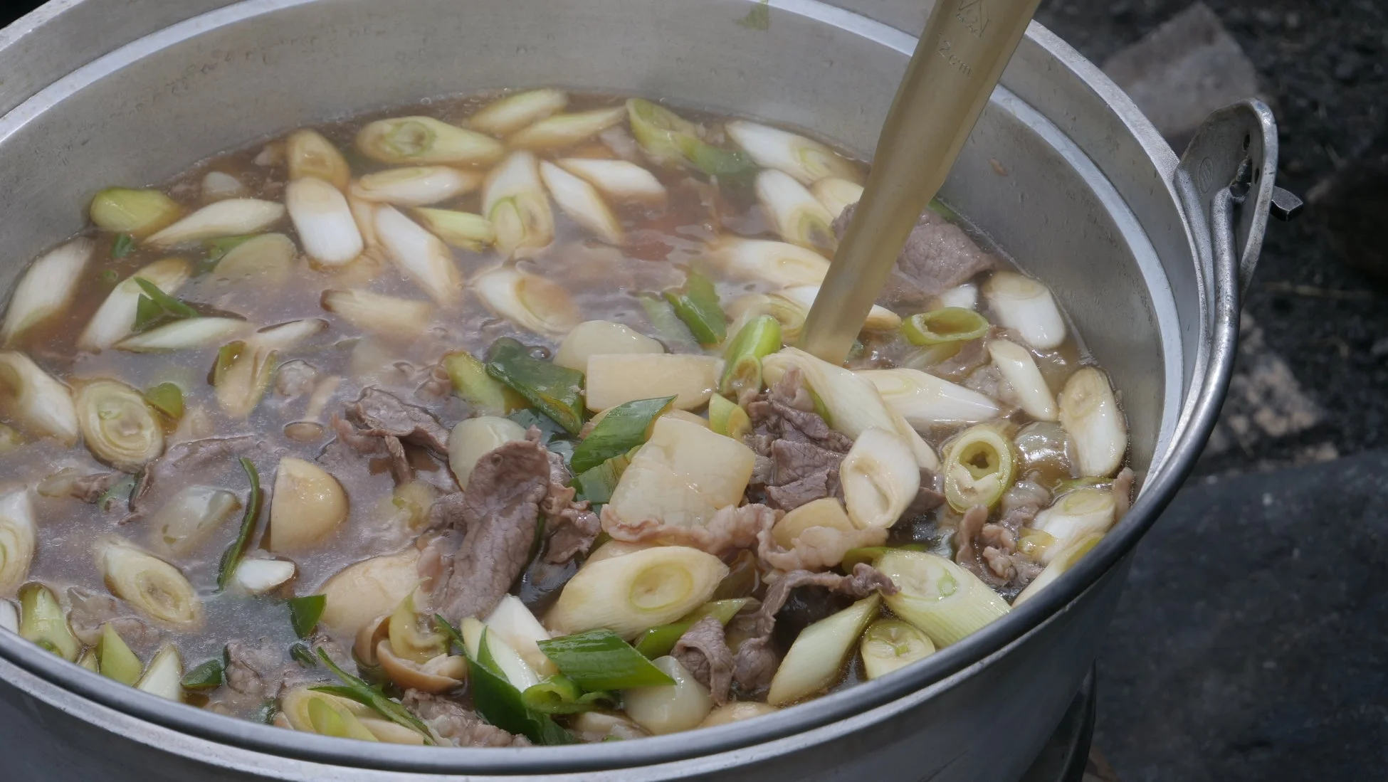 牛肉、長ネギ、野菜がたっぷり入った鍋料理が大きな鍋で調理されている様子