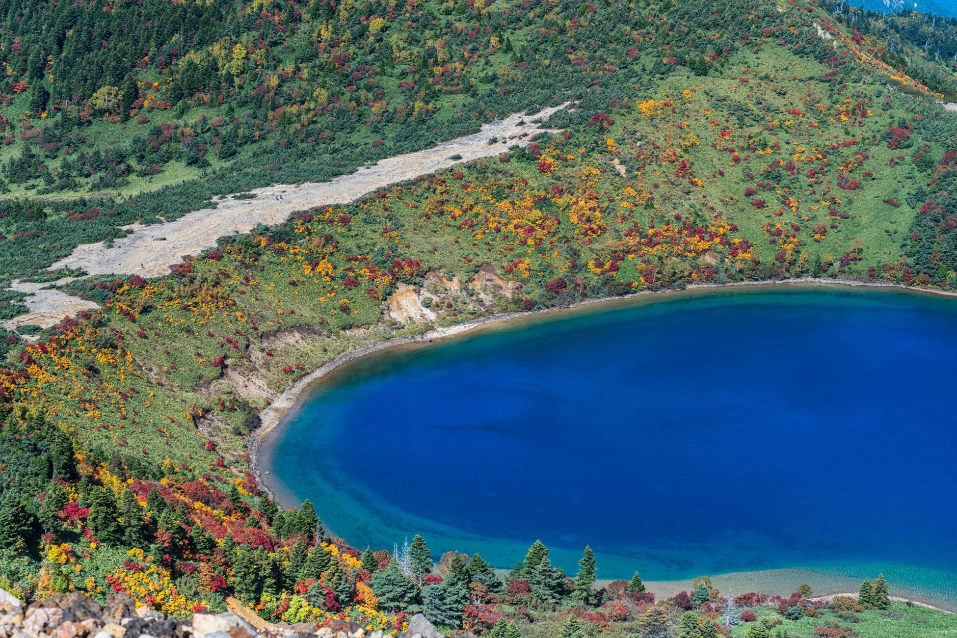 鮮やかな青い湖が、赤や黄色に色づいた紅葉の山々に囲まれている美しい秋の風景